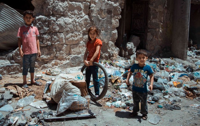 3 Kinder stehen auf einer Ruinenlandschaft in Aleppo