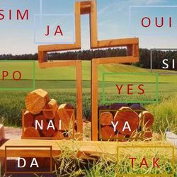 Holzkreuz in der Natur mit vielen Ja in verschiedenen Sprachen